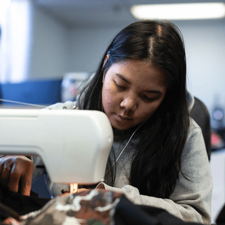 An image of one of our employees sewing on some custom neck tags on a garment.